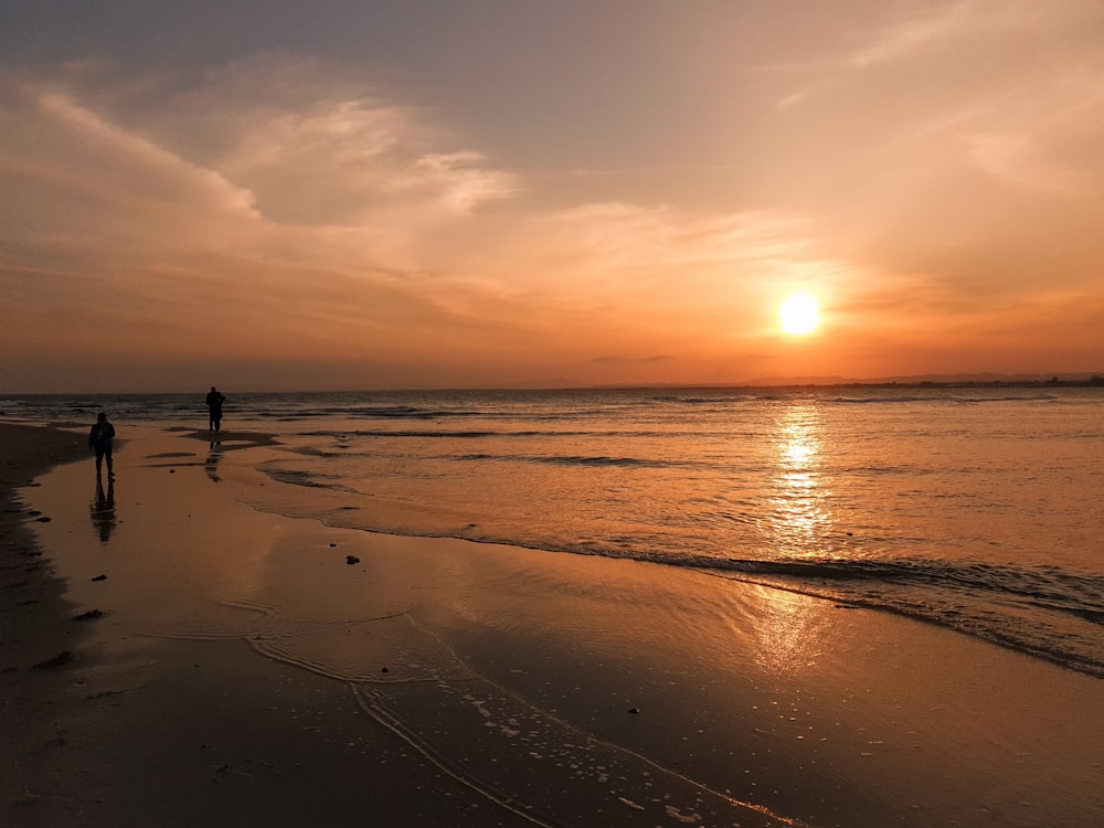 a couple of people standing on top of a beach next to the ocean