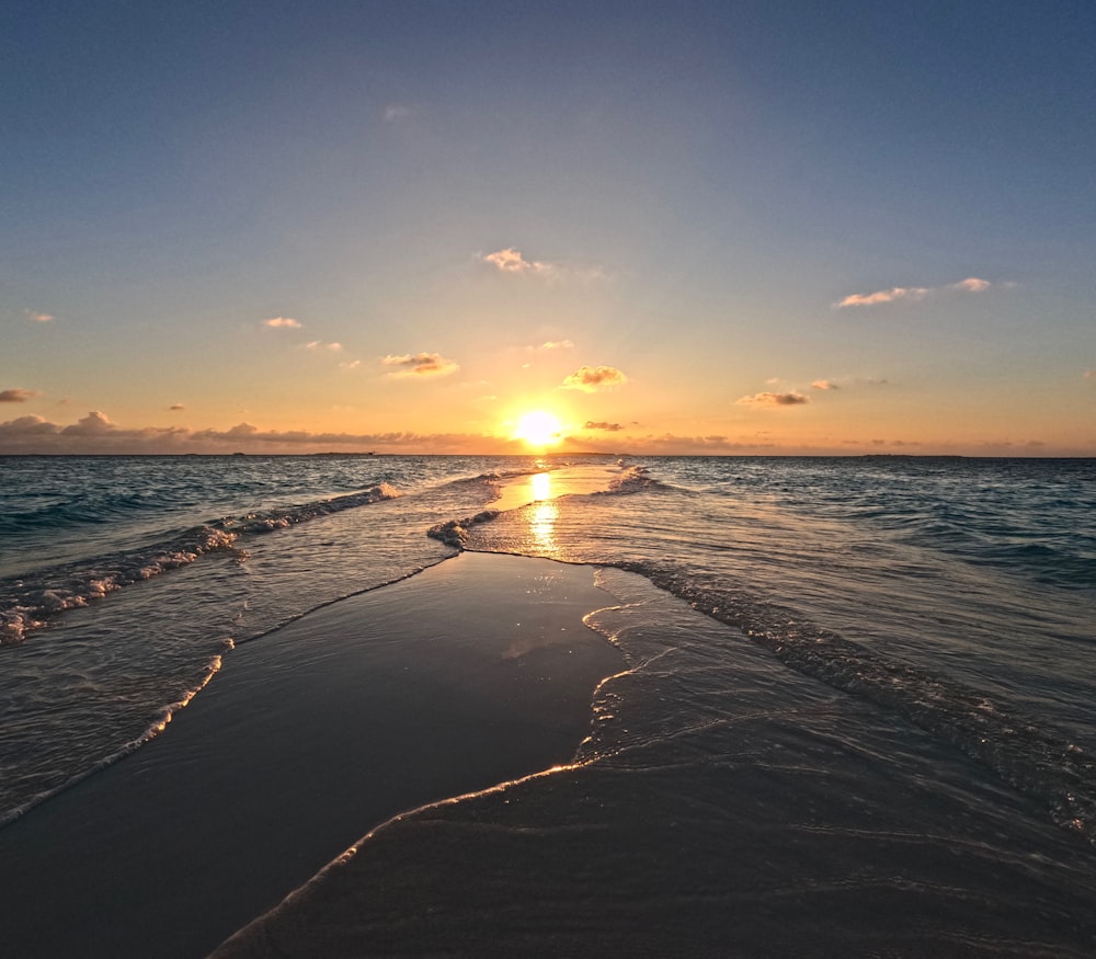 the sun is setting over the water at the beach