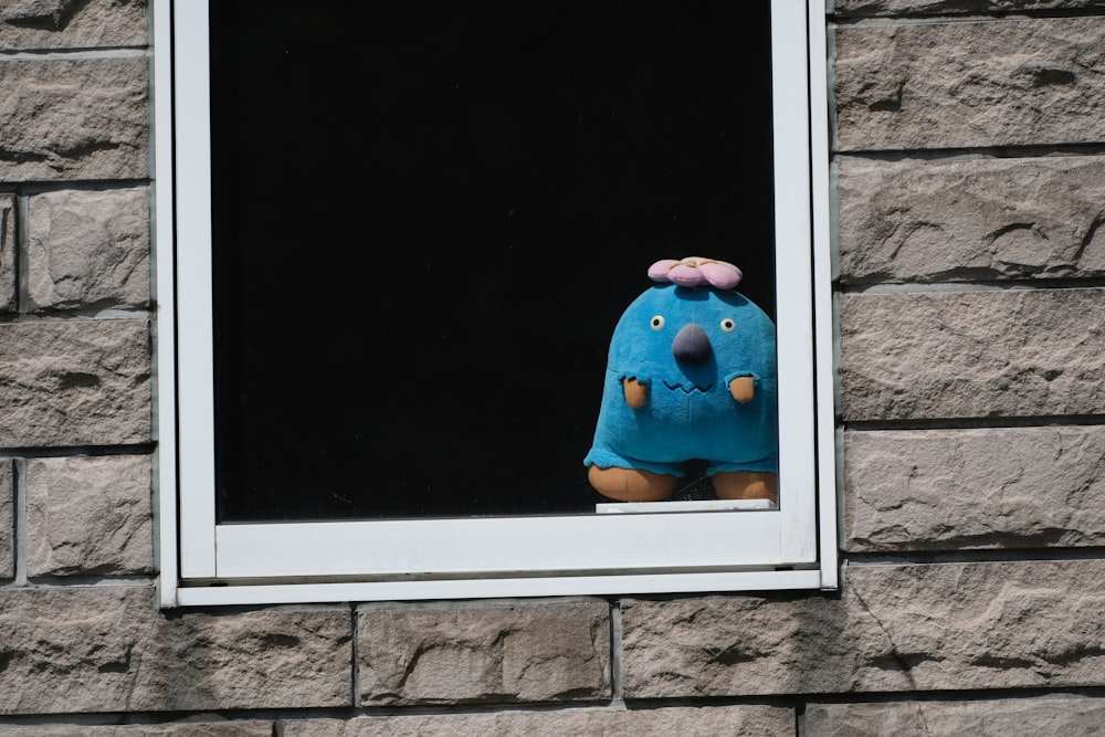 a blue stuffed animal sitting in a window sill