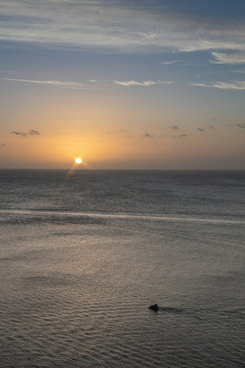 the sun is setting over the ocean with a boat in the water