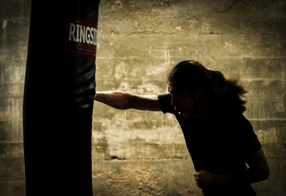 a woman in a black shirt is punching a punching bag