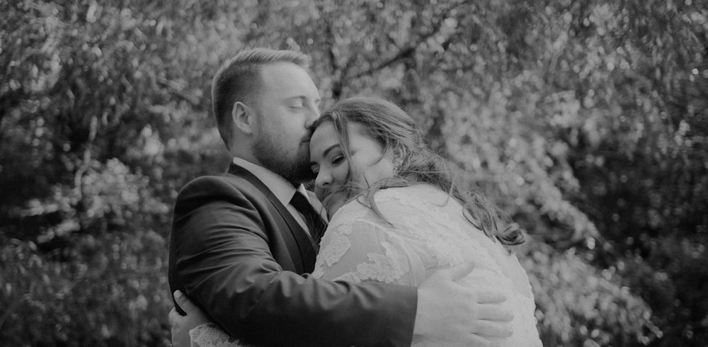 a man and a woman hugging in front of trees