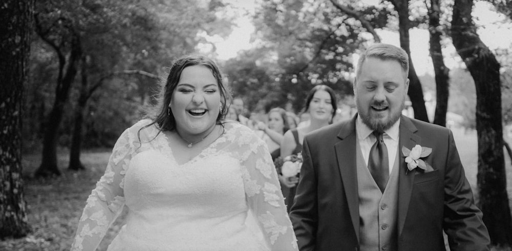 a bride and groom walking through the woods