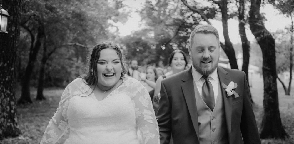 a bride and groom walking through the woods