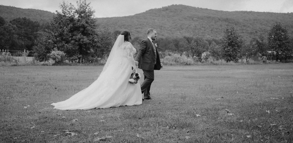 a bride and groom walking through a field