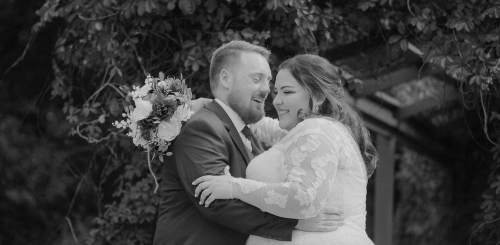 a bride and groom embracing in front of a tree