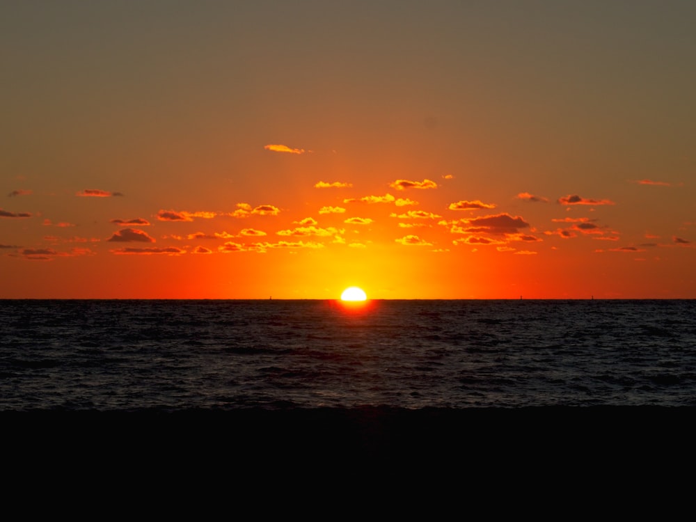 the sun is setting over the ocean on a cloudy day