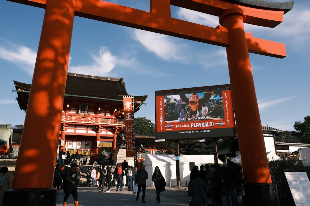 a group of people walking under a tall orange structure