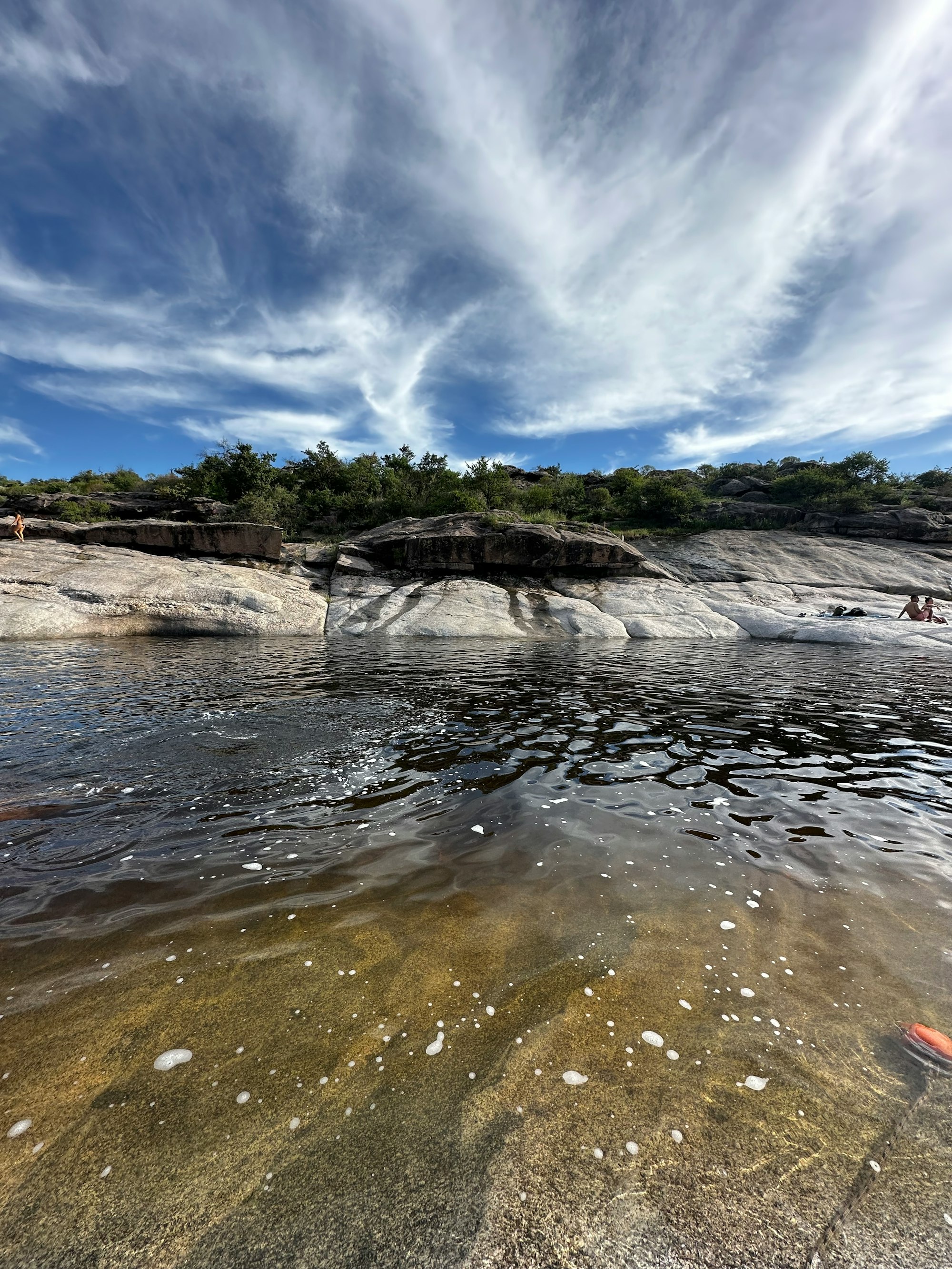 a body of water with rocks and trees in the background in Córdoba, Argentina.