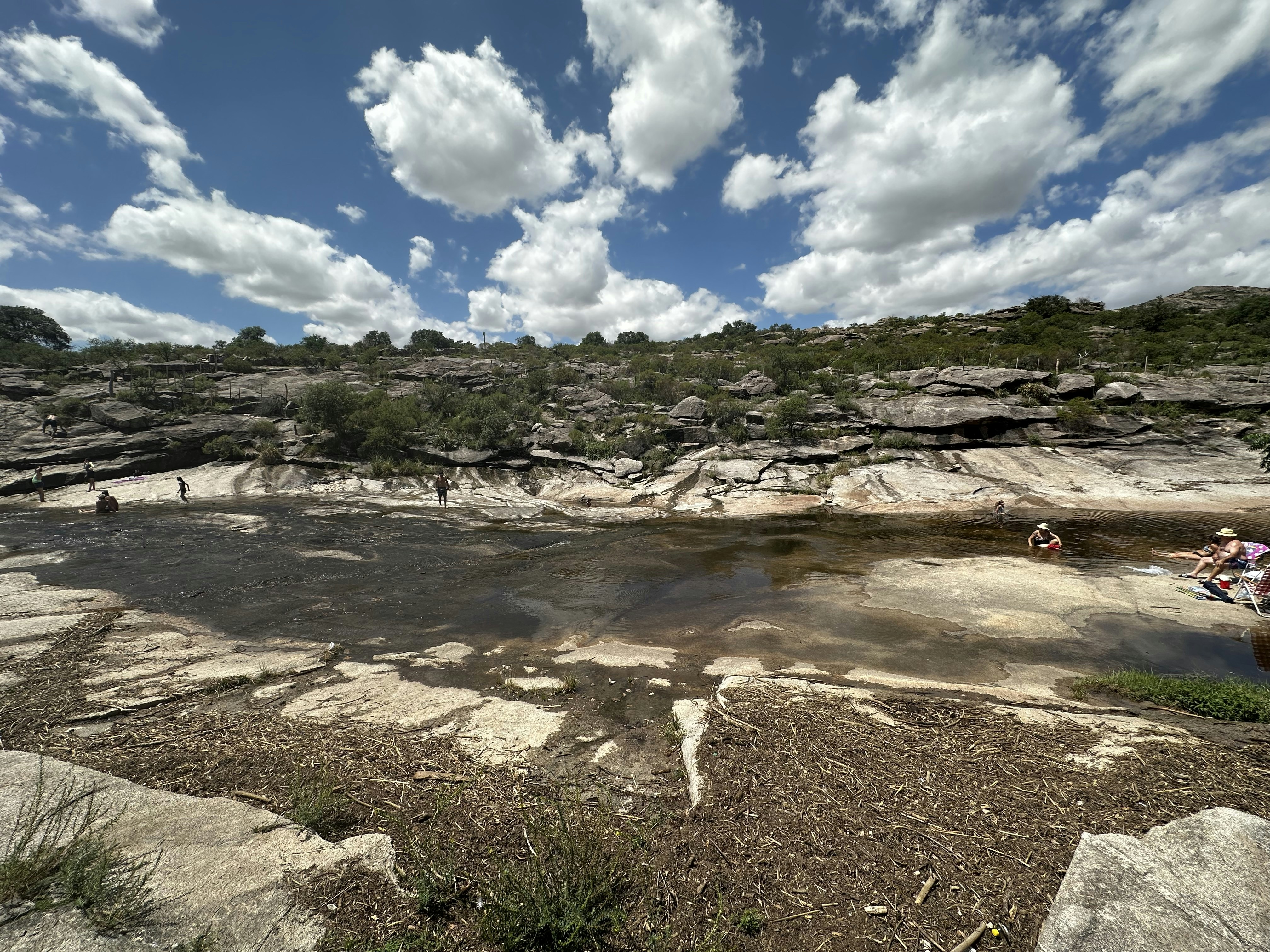 a group of people sitting on top of a rocky hillside, Tarde de verano y playa en el Valle de Traslasierra, Mina Clavero, Balneario La Toma, Provincia de Córdoba, Argentina