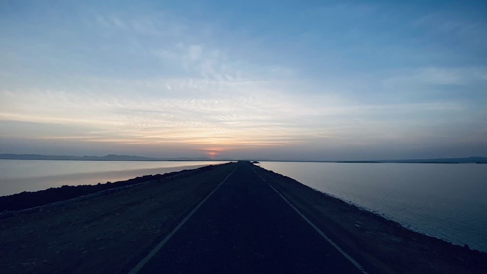 the sun is setting over the water on the road