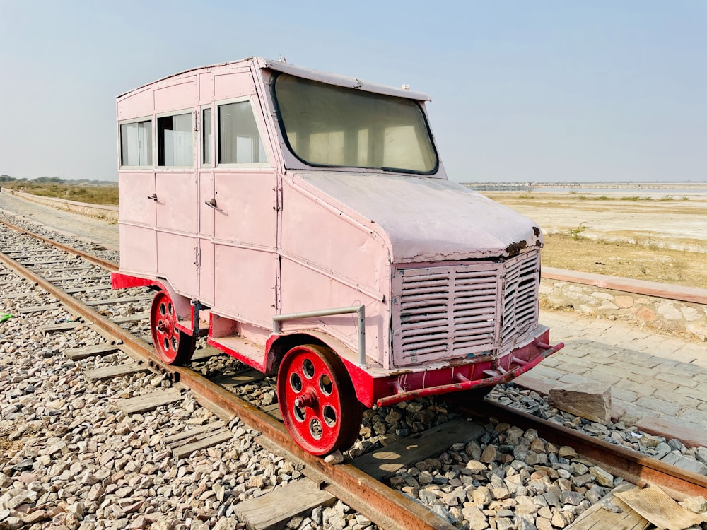 an old pink truck sitting on a train track