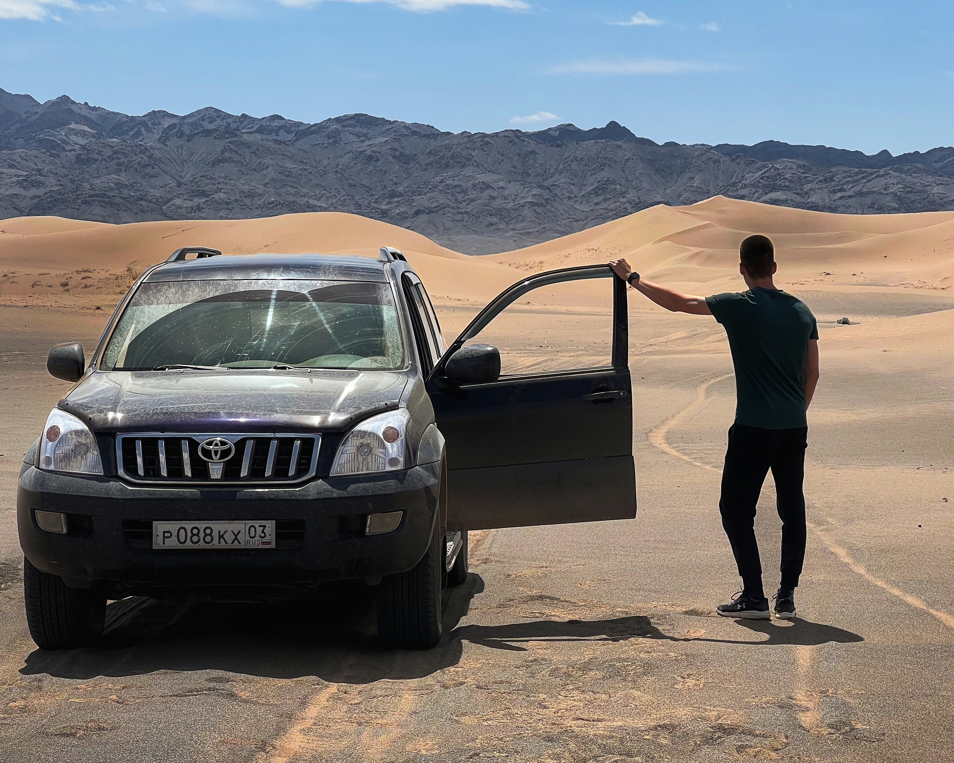 a man standing next to a car in the desert, 