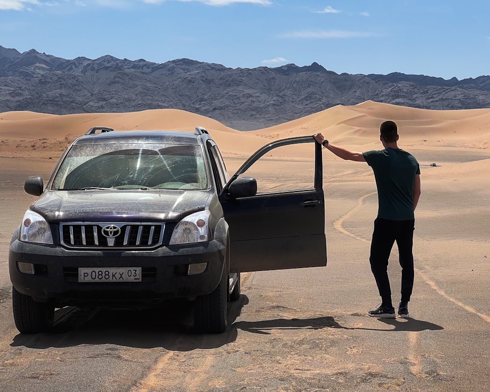 a man standing next to a car in the desert