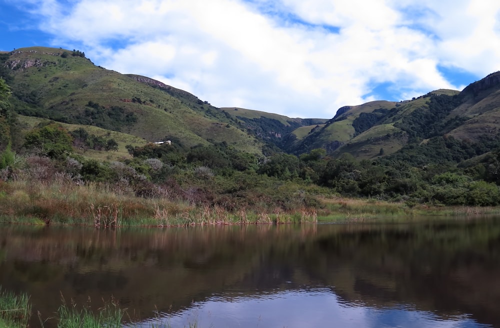 a lake surrounded by lush green mountains under a cloudy blue sky