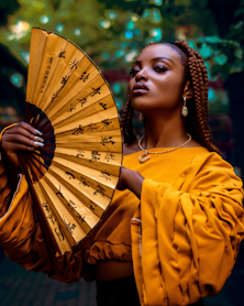 a woman with braids holding a yellow fan