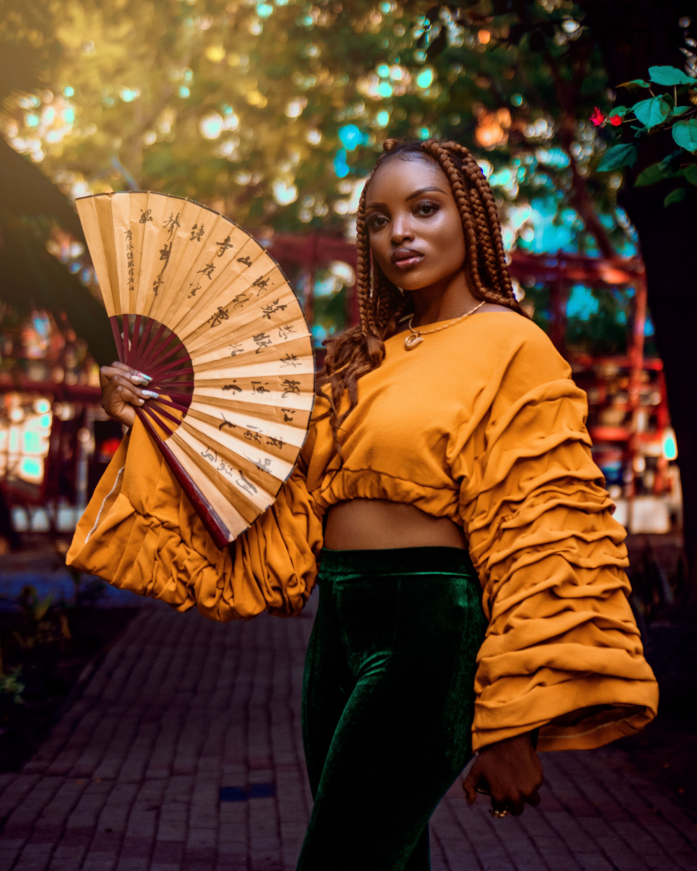 a woman in a yellow top and green pants holding a fan