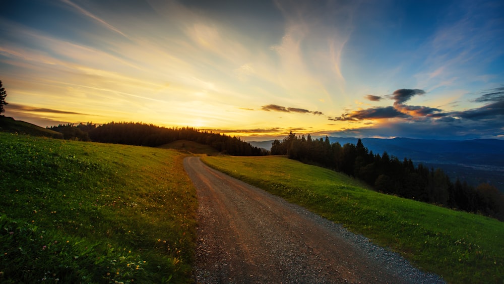 un camino de tierra que sube una colina con una puesta de sol de fondo