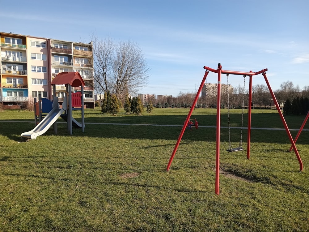 a red swing set in a park with a building in the background