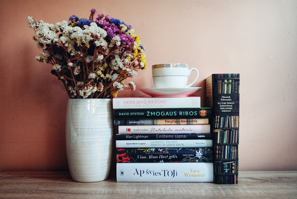 a stack of books sitting next to a vase filled with flowers