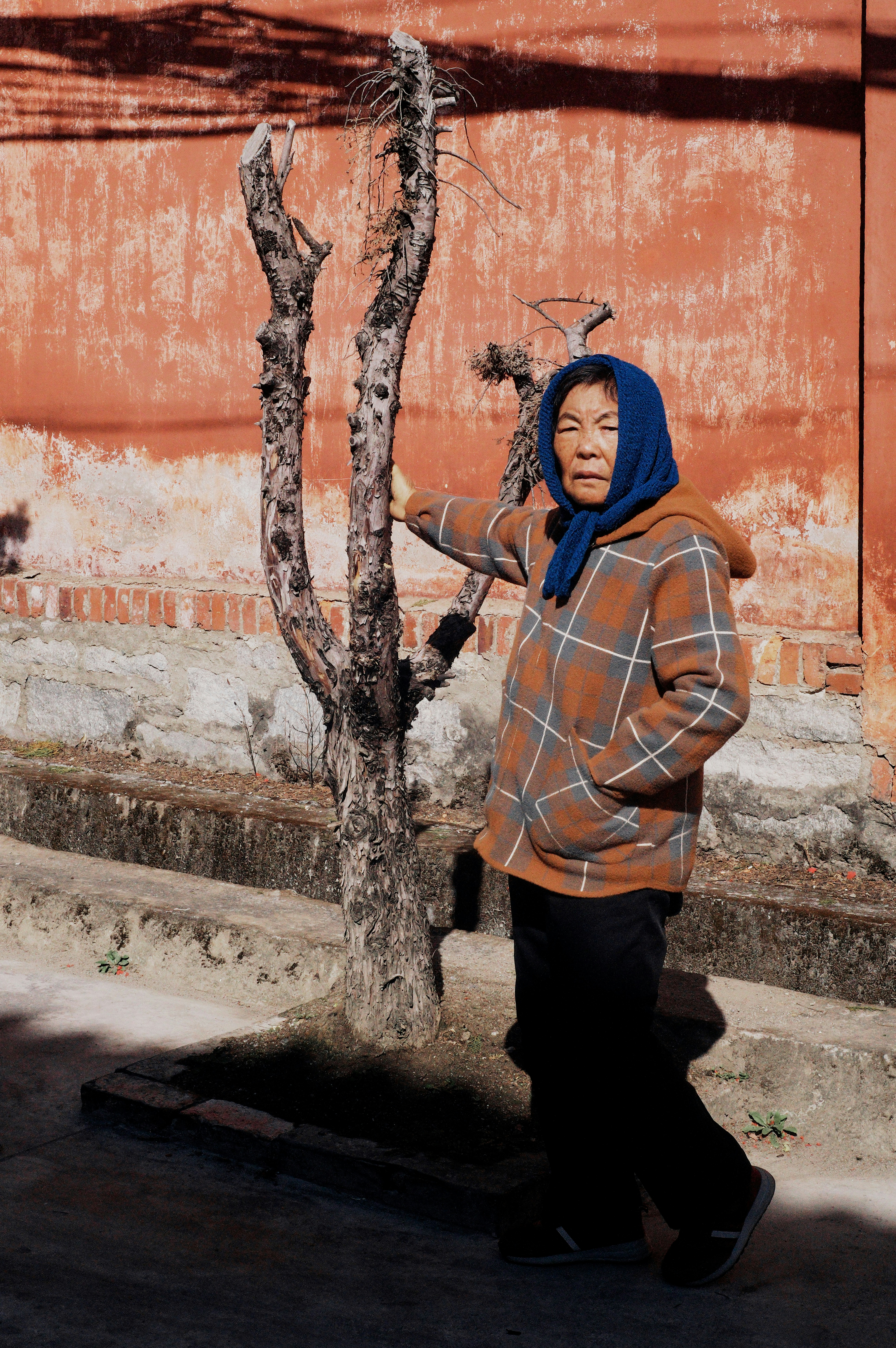 a woman standing next to a tree in front of a building