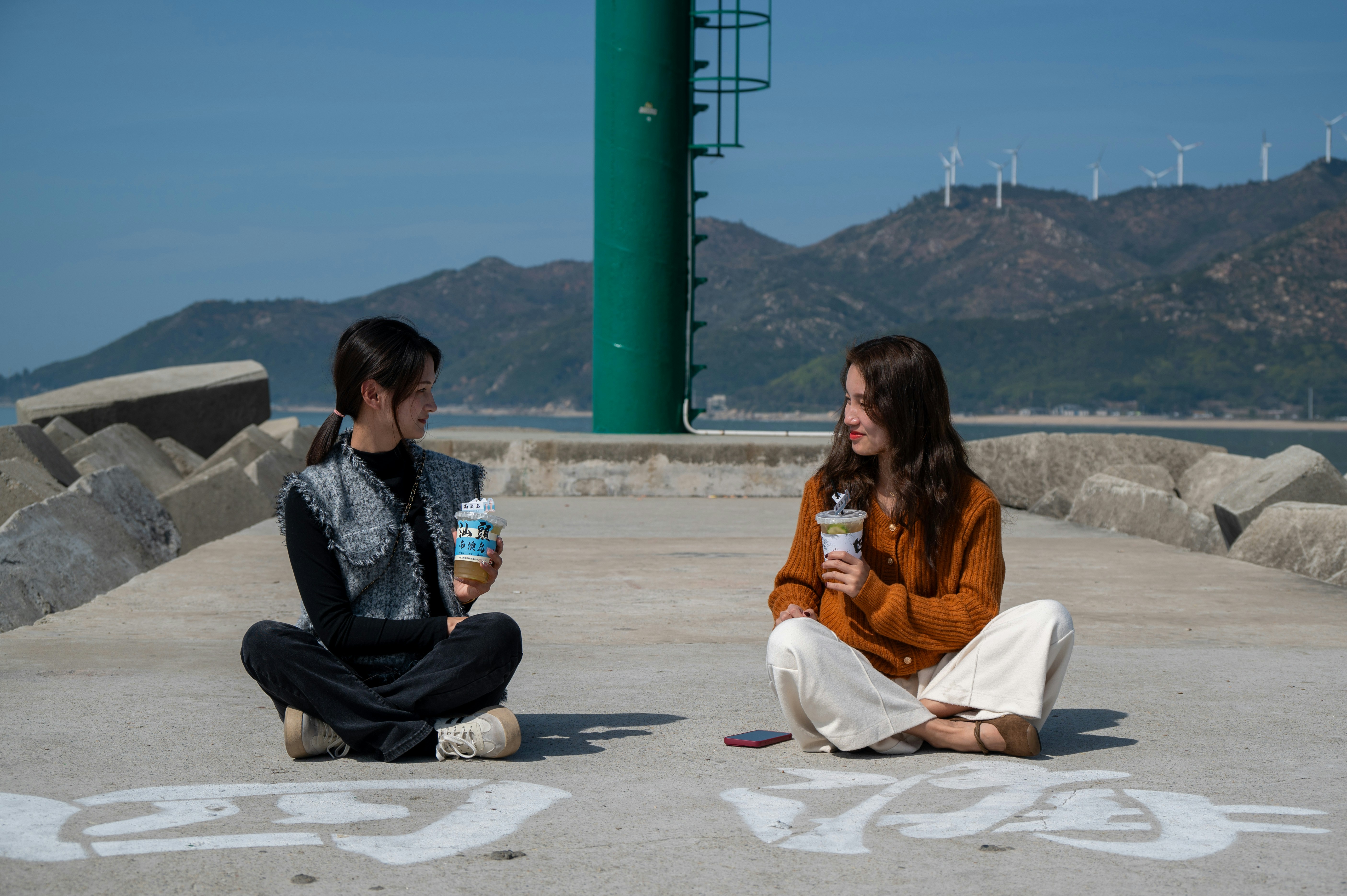 two girls sitting on the ground drinking coffee