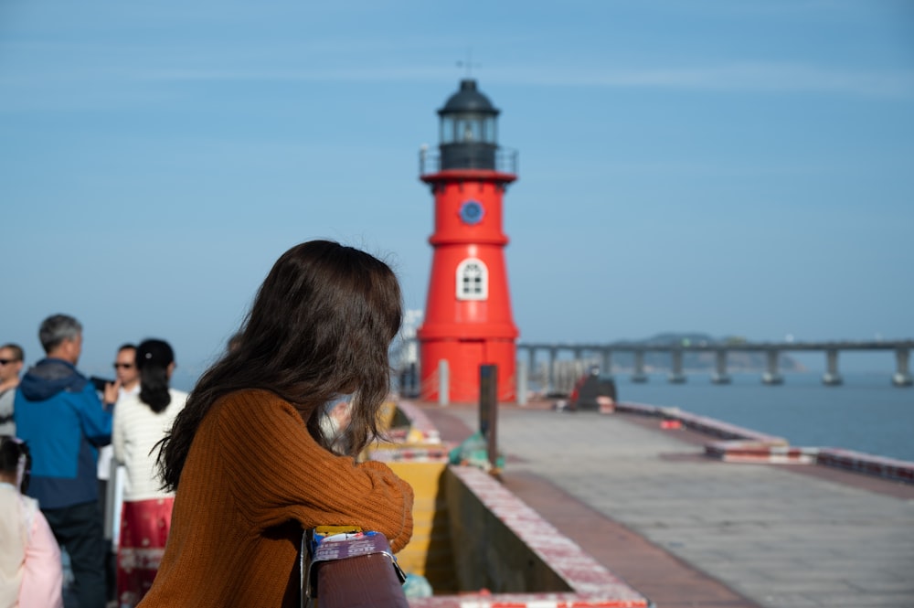a group of people standing on a pier next to a red light house
