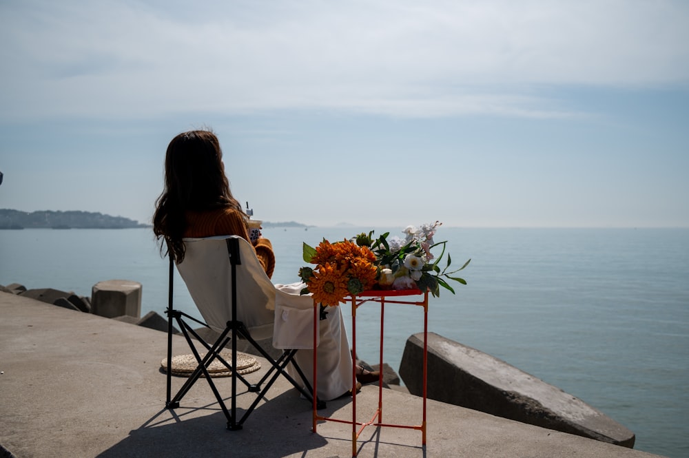 a woman sitting in a chair next to a table with flowers on it