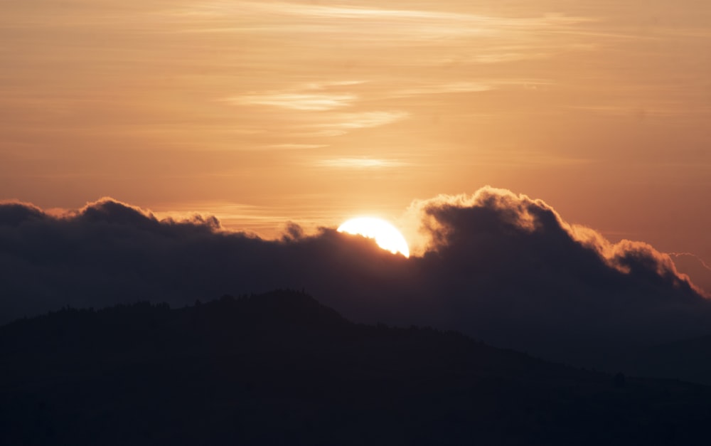 the sun is setting behind a cloud covered mountain