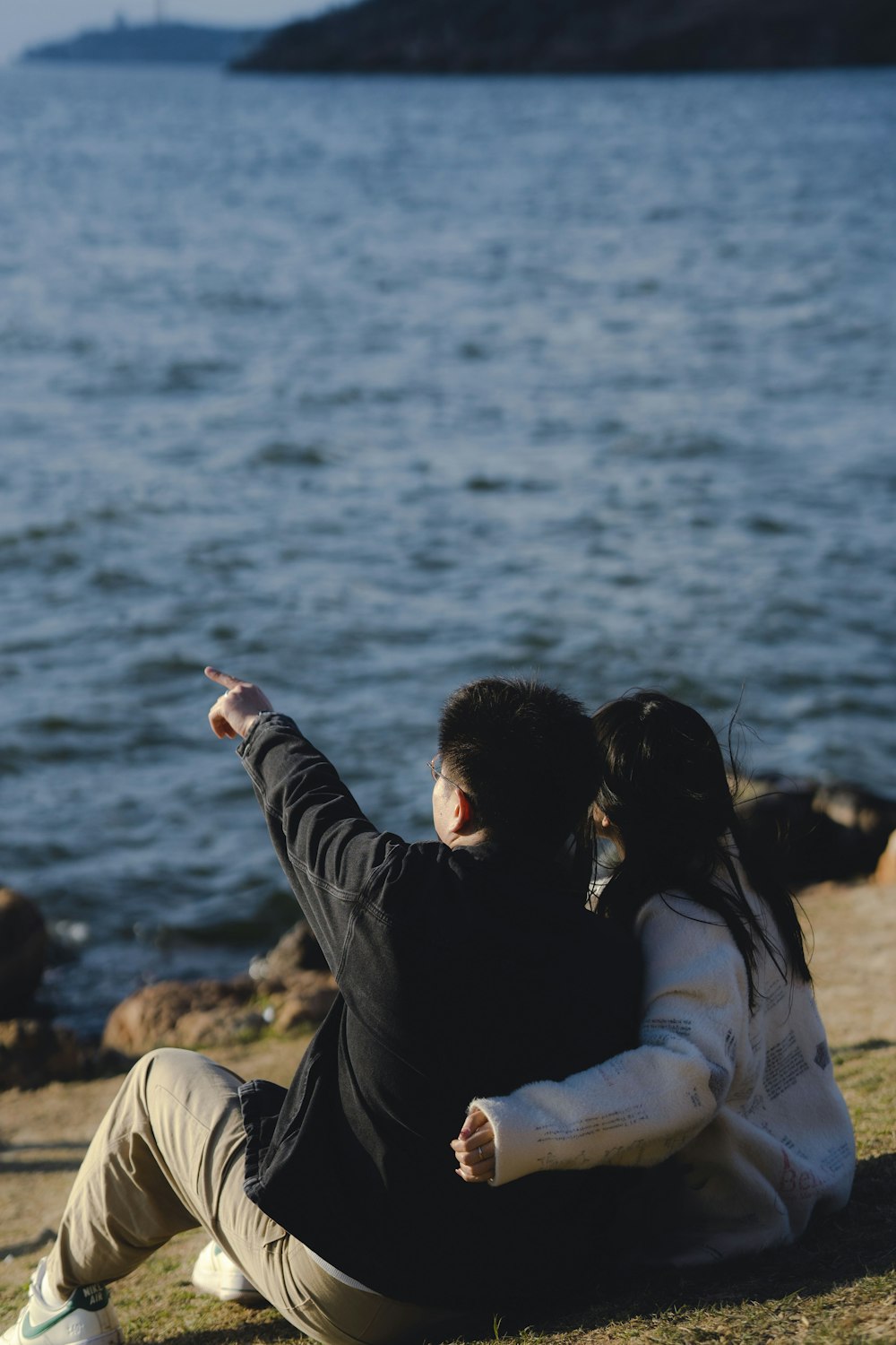 a man and a woman sitting on the ground by the water
