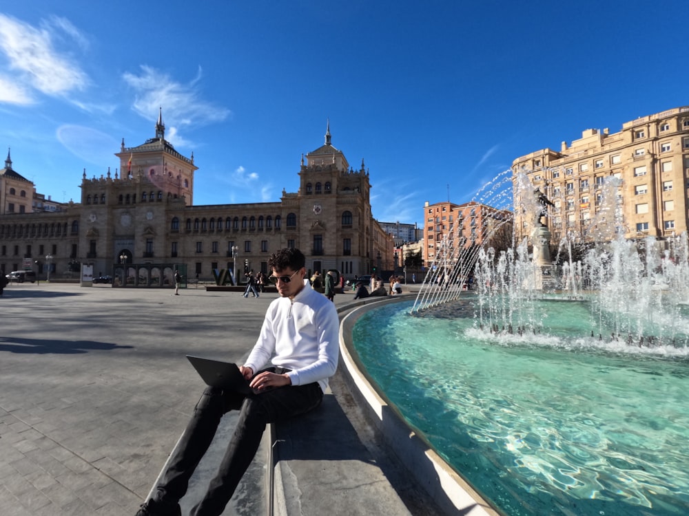 a man sitting on a ledge next to a fountain