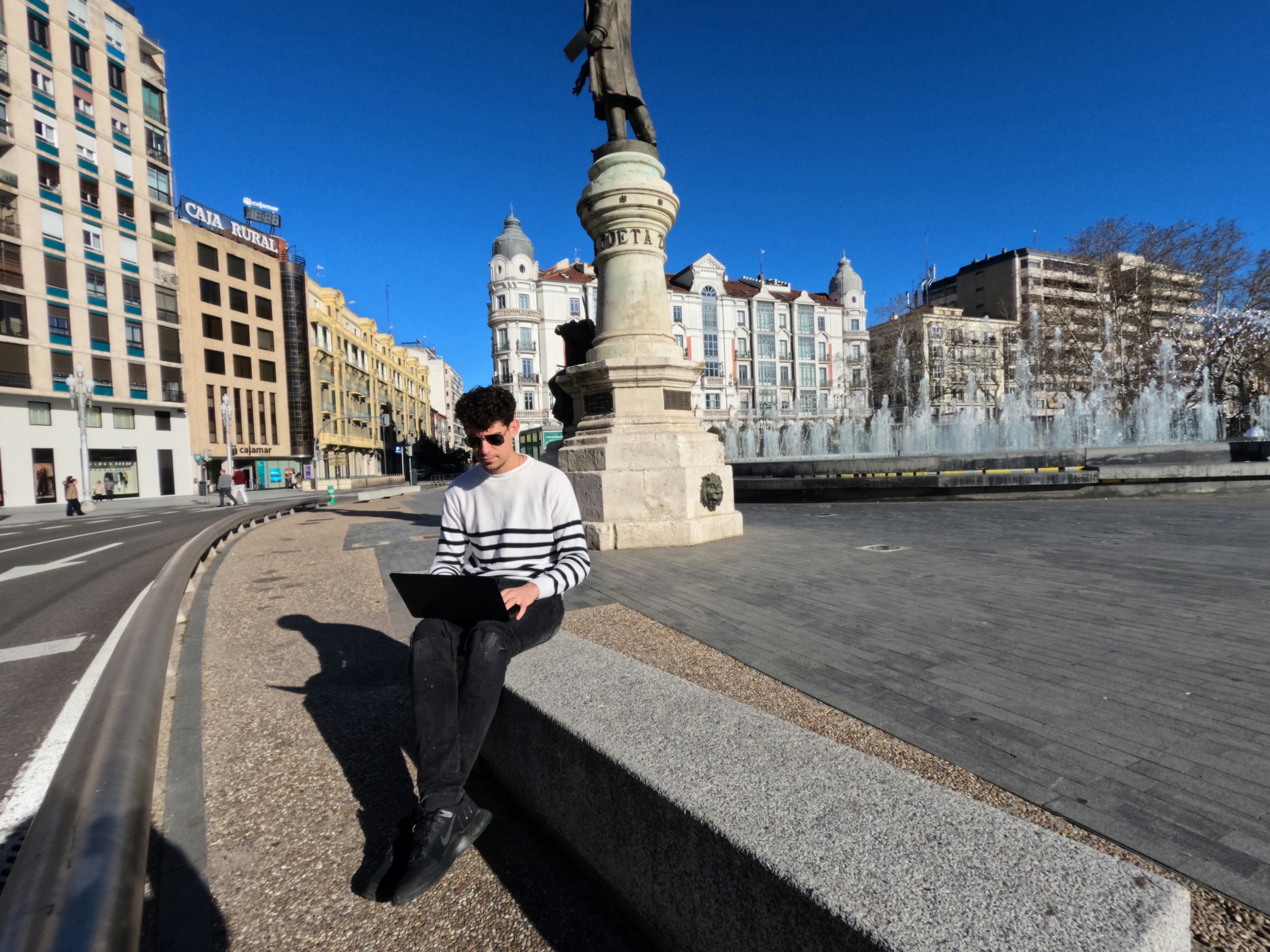 a man sitting on a ledge using a laptop computer