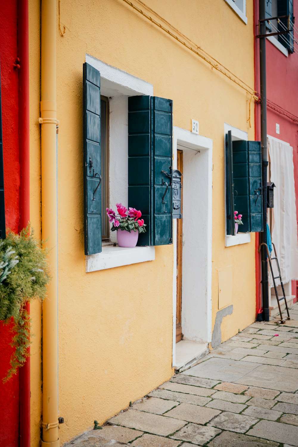 a yellow building with green shutters and flowers in a window