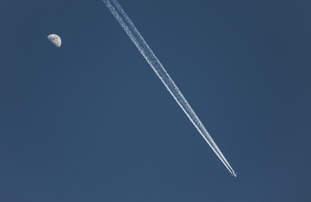 a contrail flying in the sky with a moon in the background