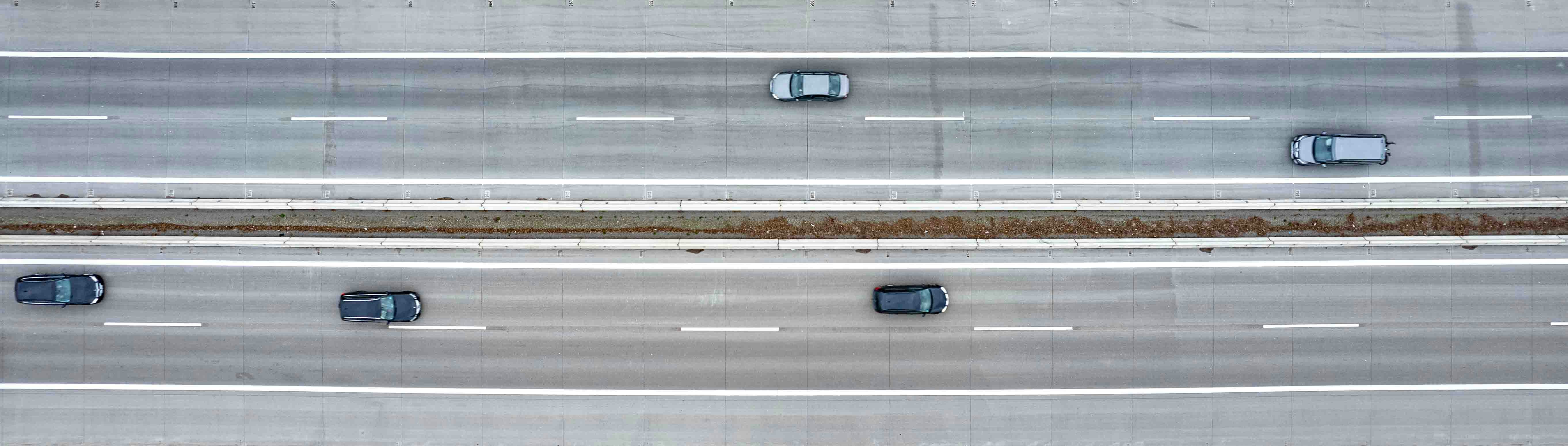 an overhead view of three lanes of a highway, The photograph from above freezes a moment on the highway, where cars and lanes are depicted in a clean composition, reflecting a slice of daily movement and travel.