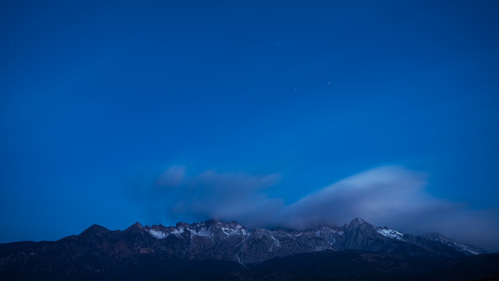 the night sky with clouds and mountains in the background