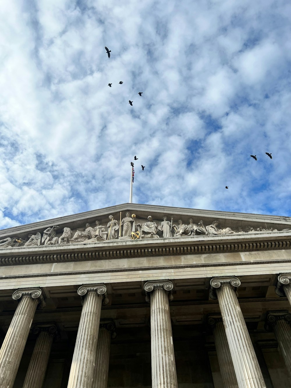 a building with columns and birds flying in the sky