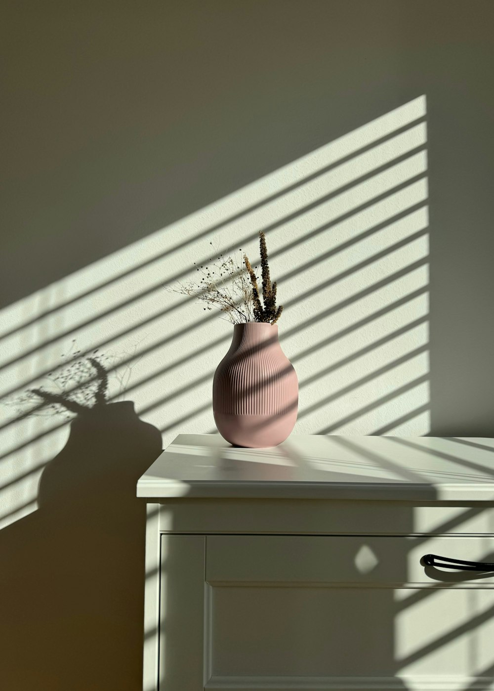 a pink vase sitting on top of a white dresser