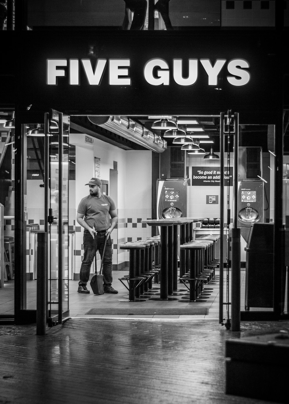 a black and white photo of a man standing in front of a five guys store