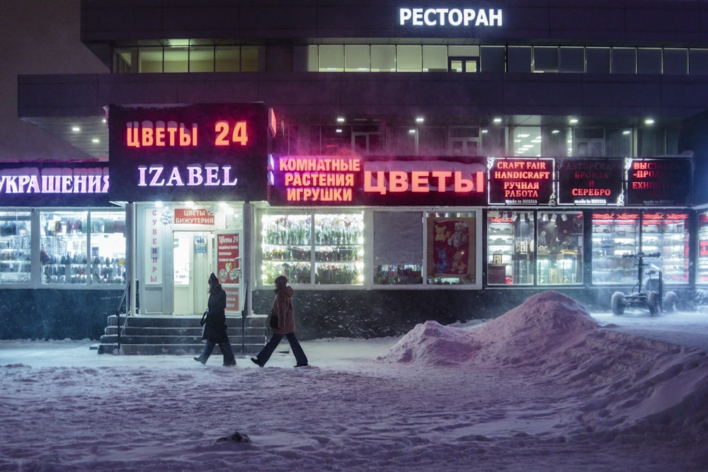 two people walking in the snow in front of a store