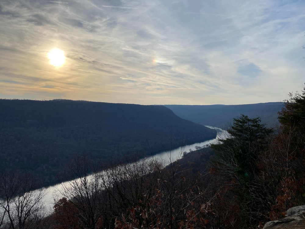 the sun is setting over a river in the mountains