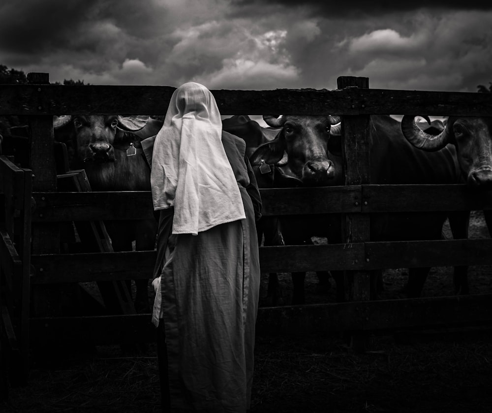 a black and white photo of a woman standing in front of cows