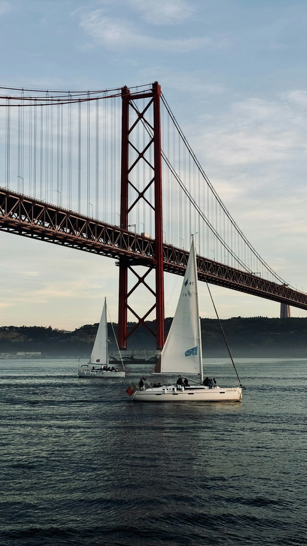 two sailboats in the water under a bridge