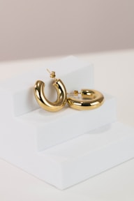 a pair of gold hoop earrings on a white stand
