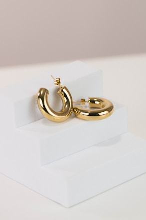 a pair of gold hoop earrings on a white stand