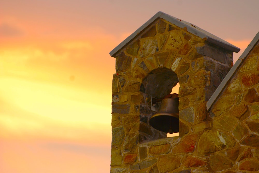 a bell on the side of a building with a sunset in the background