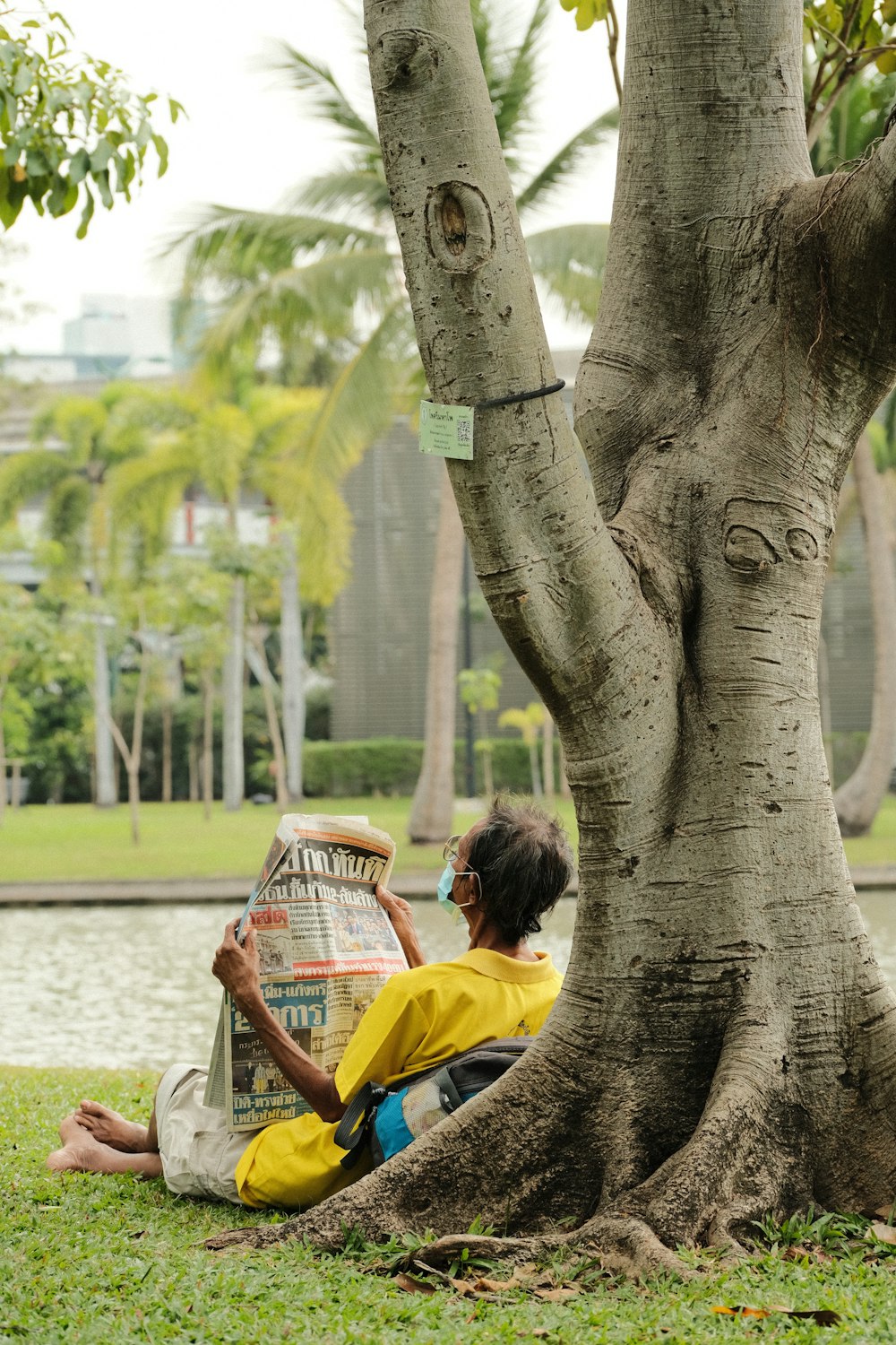 a person sitting under a tree reading a newspaper