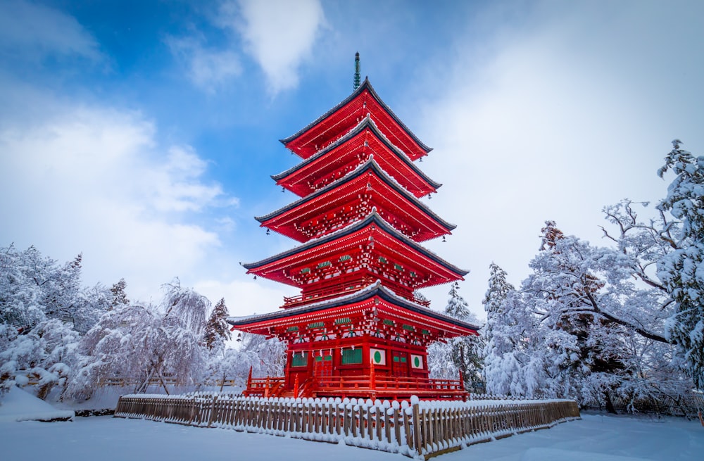 a tall red pagoda in the middle of a snow covered forest