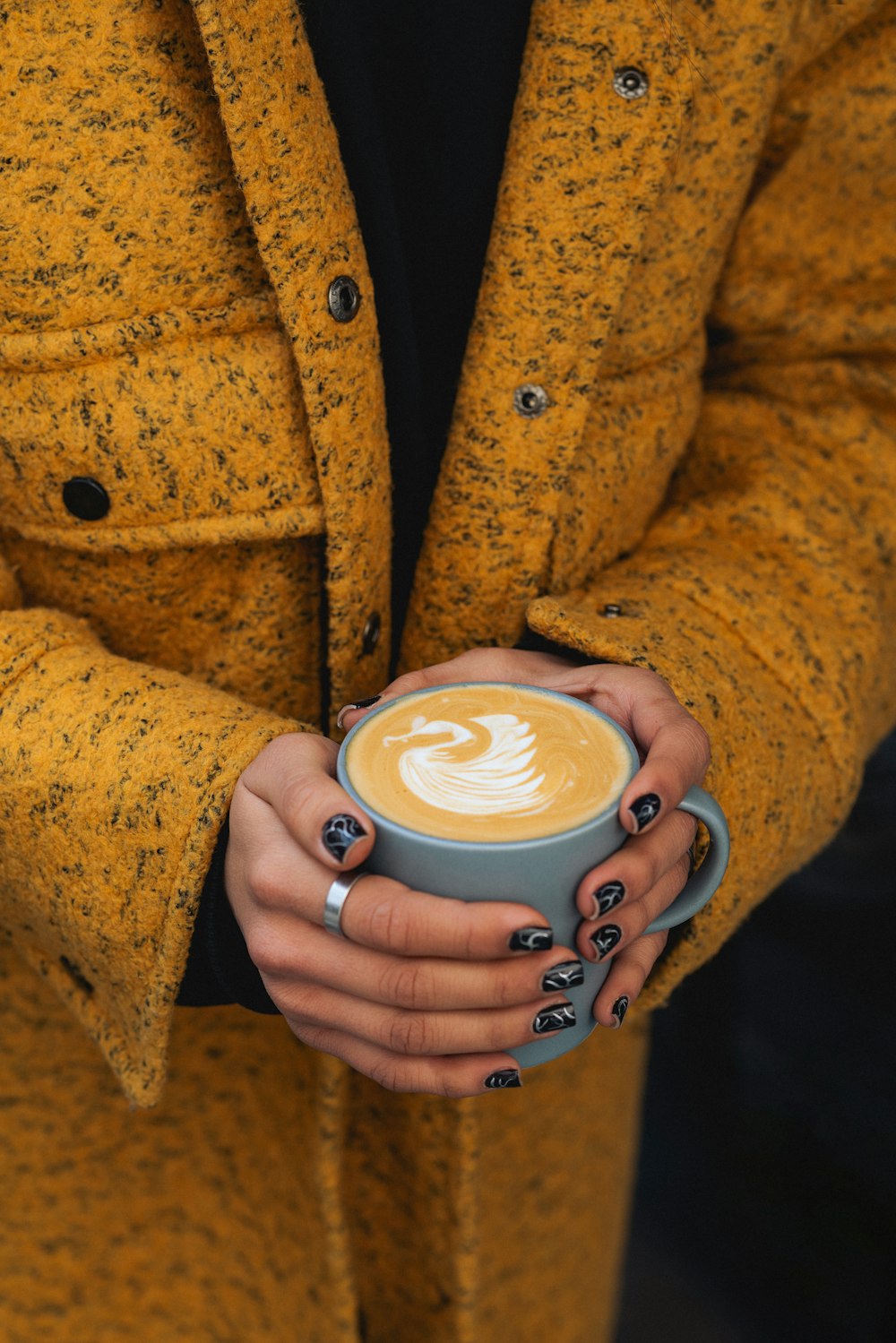 a woman in a yellow coat holding a cup of coffee