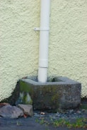 a white pipe sticking out of the ground next to a wall